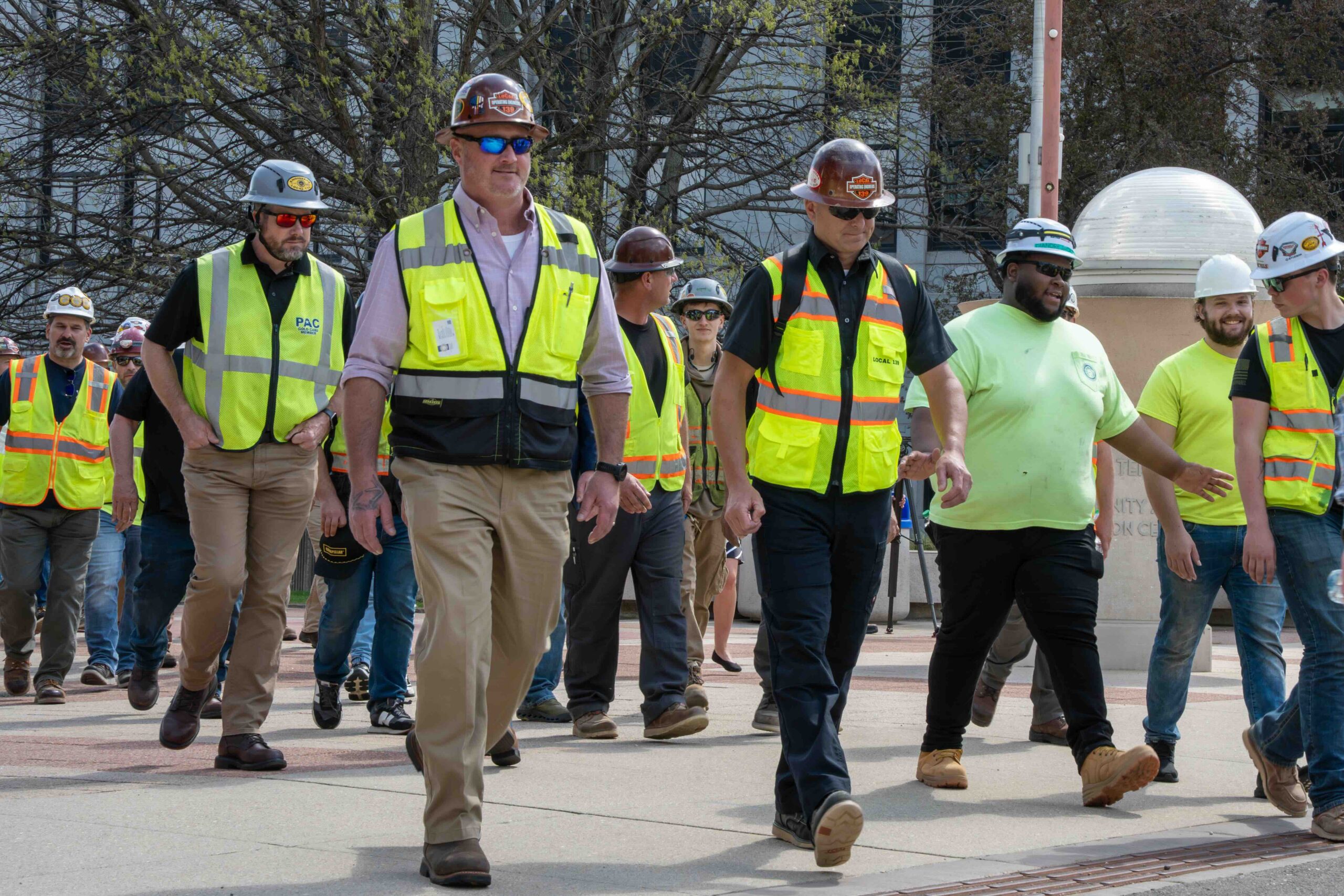 Group of construction workers walking together in safety vests and hard hats outdoors on a sunny day.