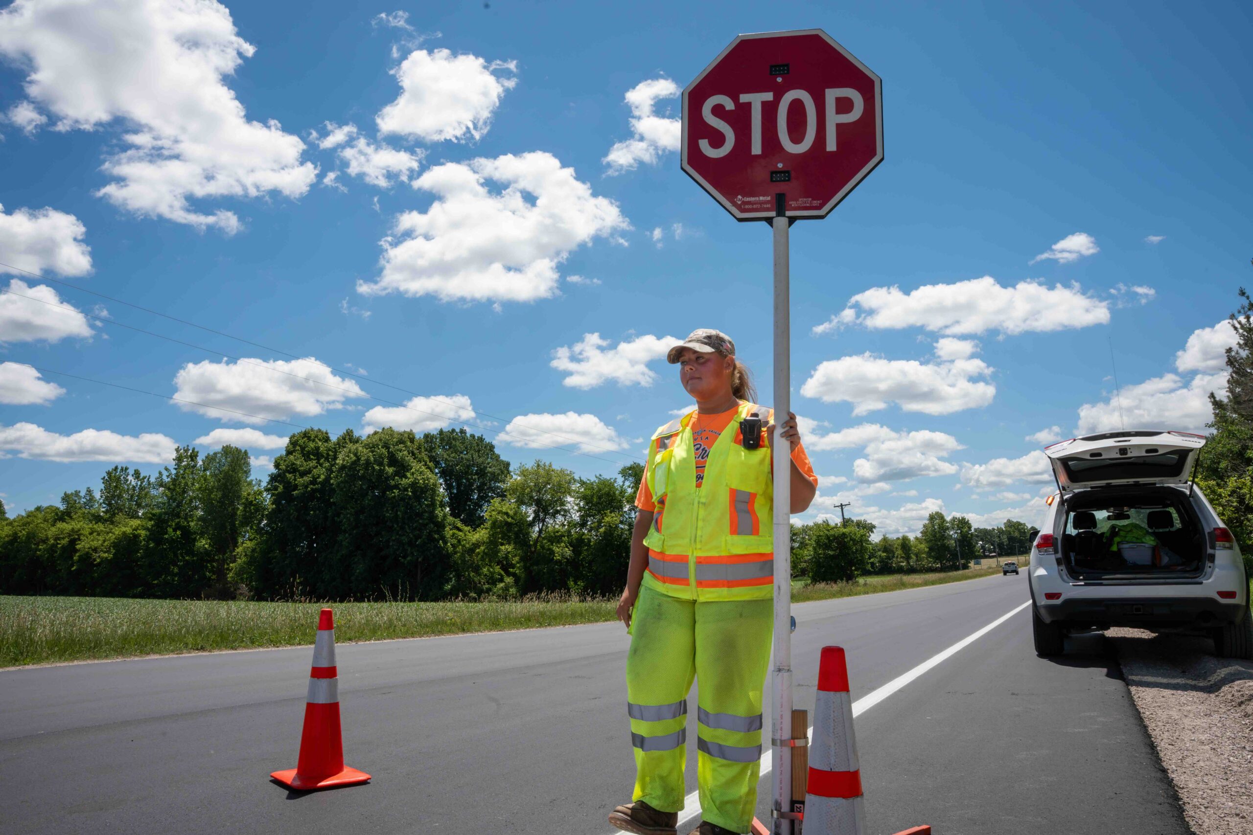 Road construction worker in a neon vest holding a STOP sign beside orange traffic cones on a sunny day.