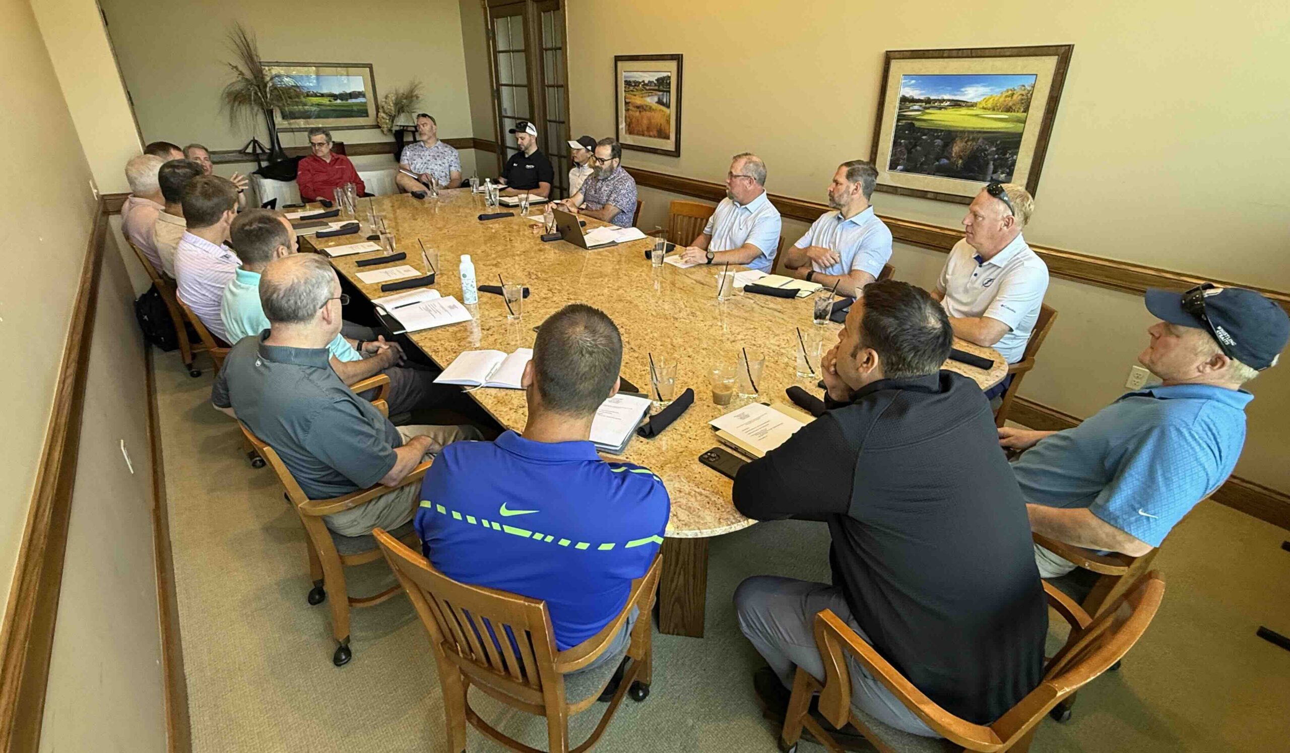 Conference room meeting with adults around a long table, documents and laptops visible, discussing a project.