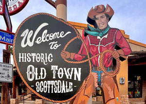 Colorful storefront with a round sign that says 'Welcome to Historic Old Town Scottsdale' and a life-sized cowboy cutout beside it.